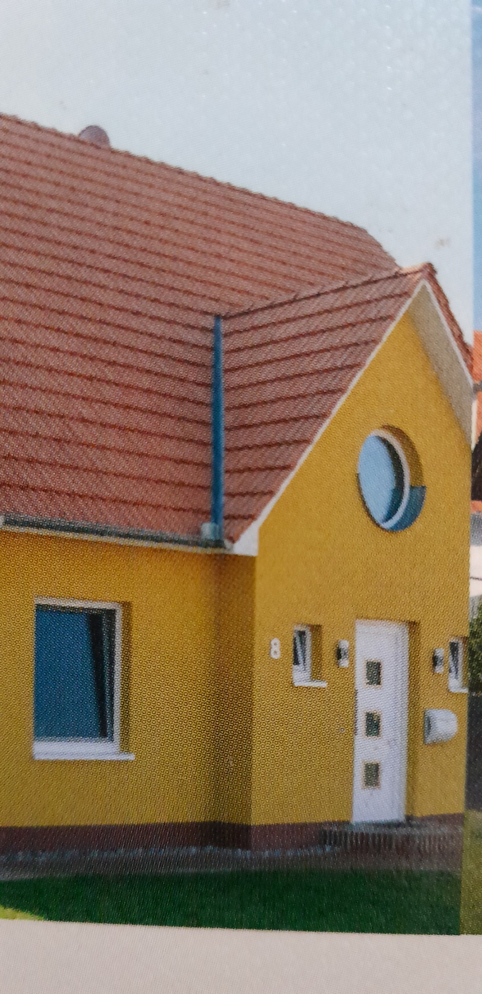 Żółty dom z okrągłym oknem i brązowym dachem z dachówki.