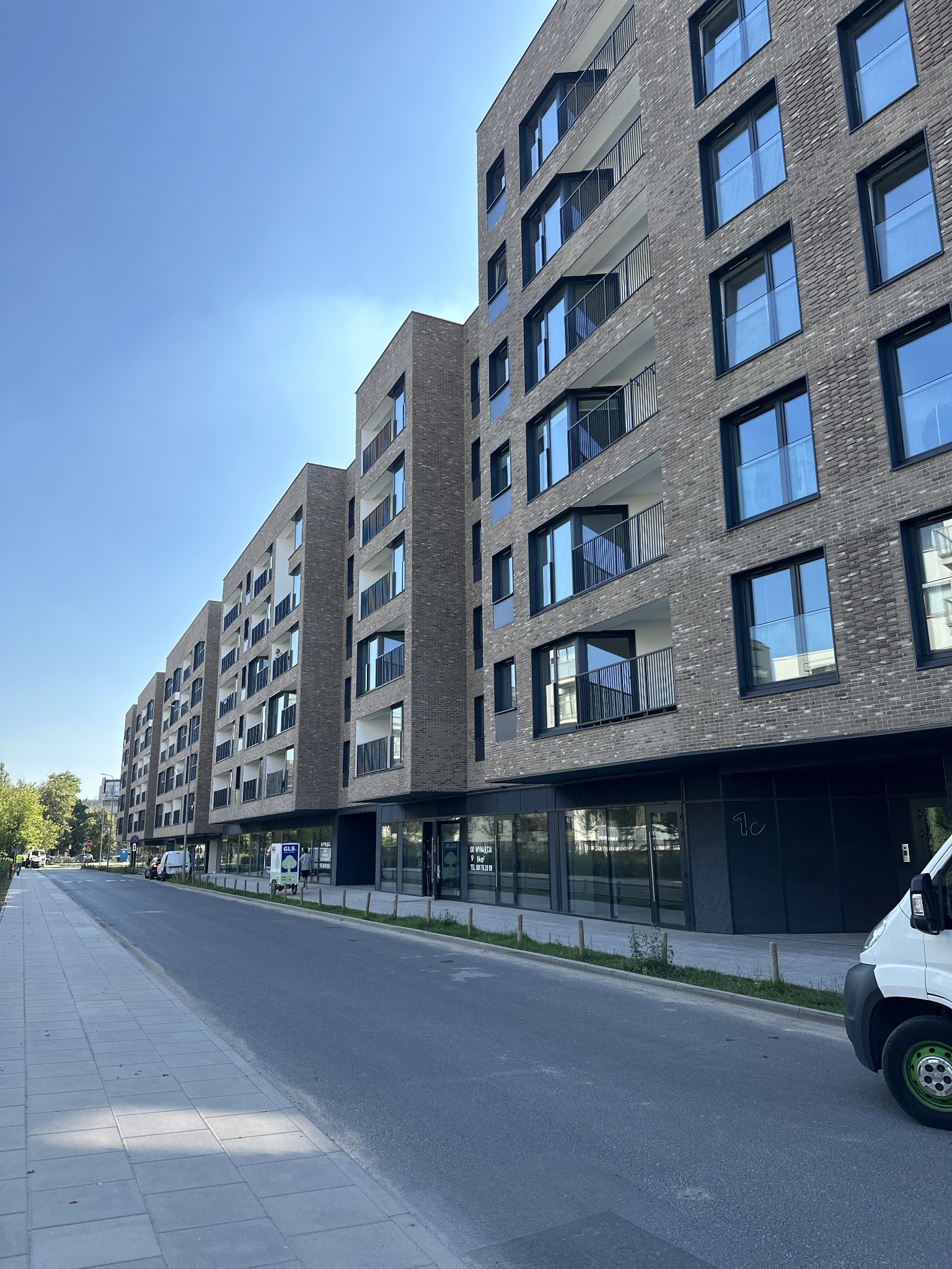 Nowoczesny budynek wielorodzinny z szarej cegły z balkonami z metalowymi balustradami i dużymi oknami, widok z poziomu ulicy w słoneczny dzień.