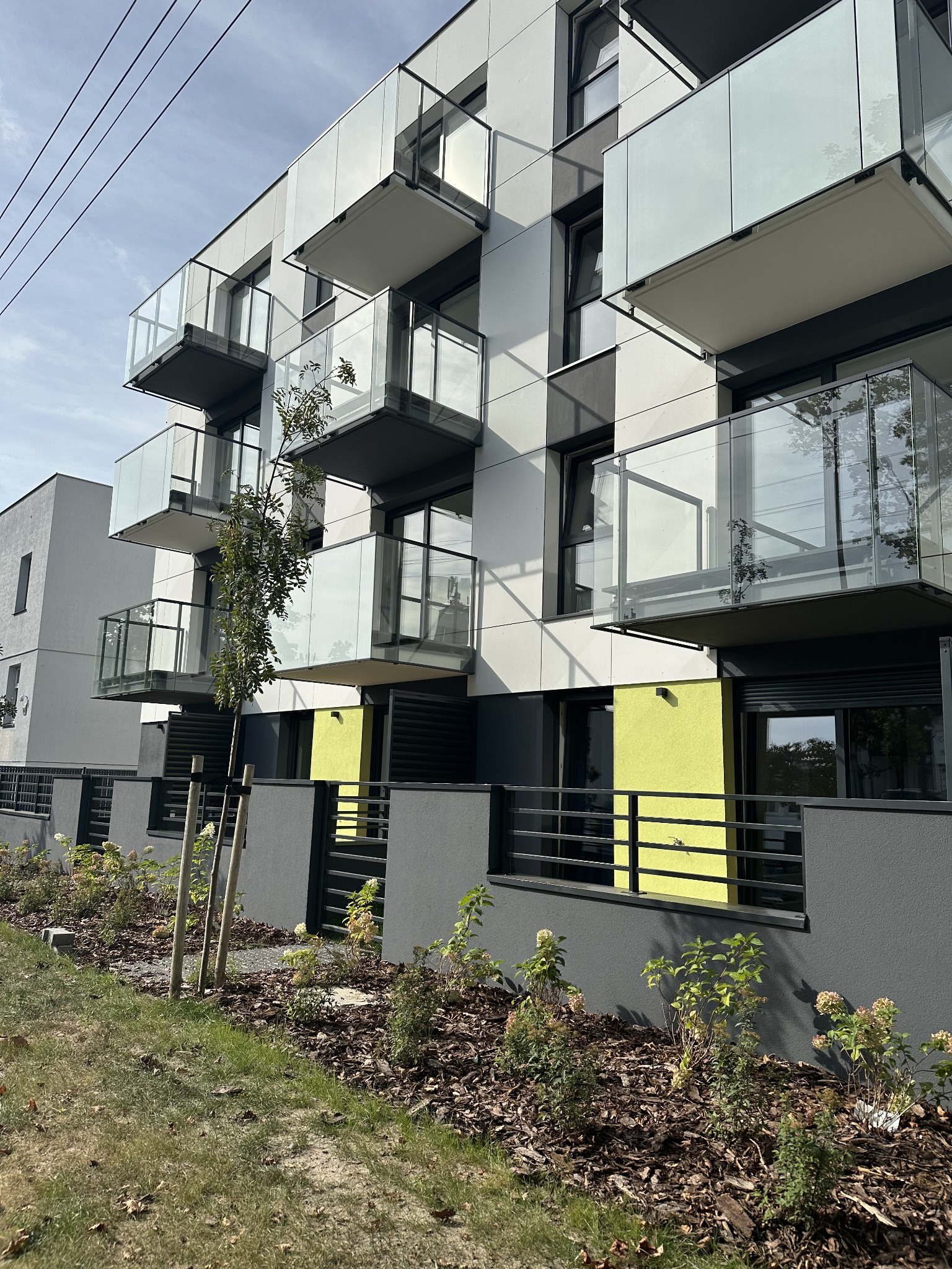 Nowoczesny budynek wielorodzinny z balkonami z balustradami ze szkła, widok z poziomu gruntu na fasadę z elementami w kolorze limonkowym.