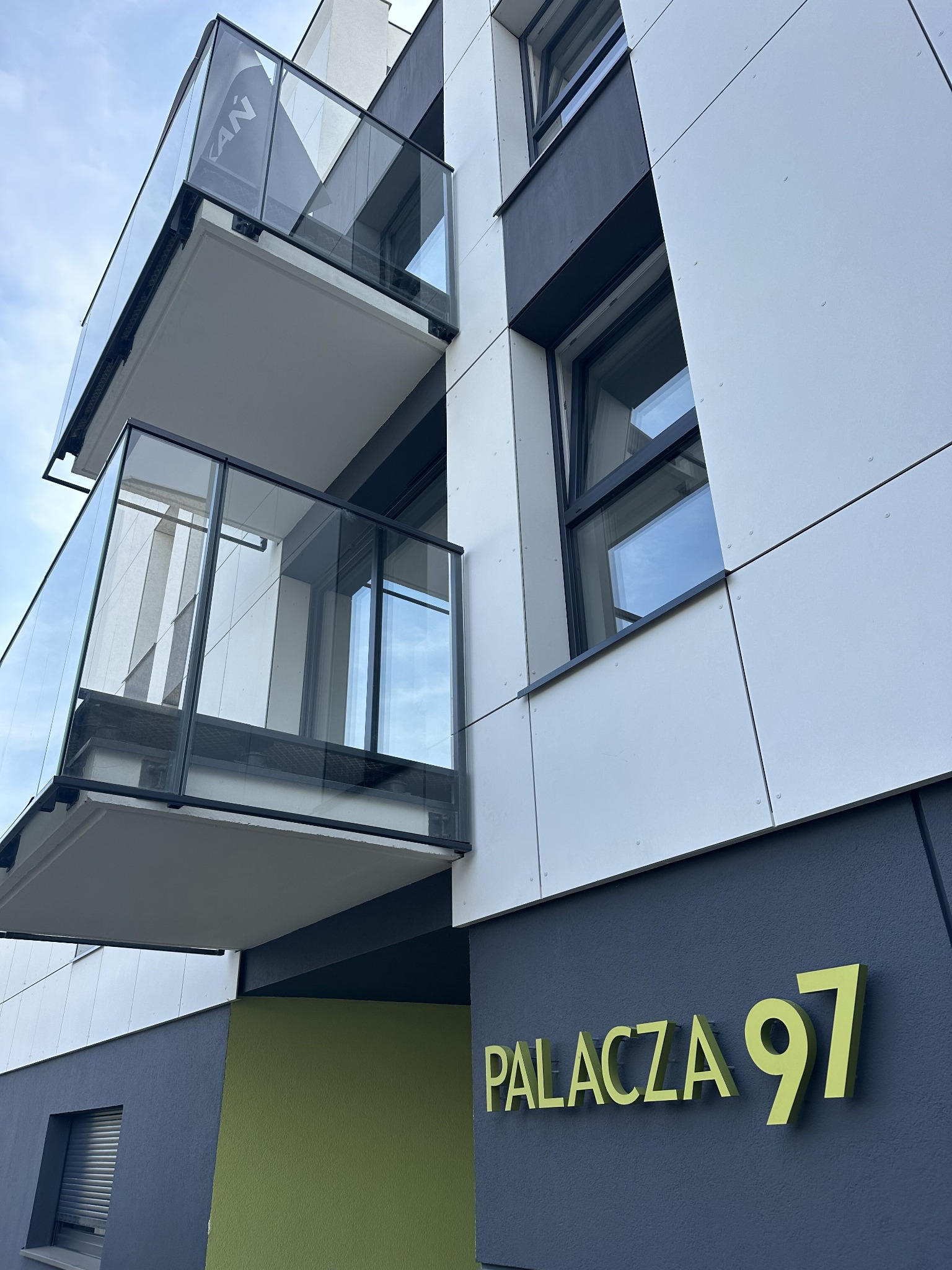 Nowoczesny budynek mieszkalny w Poznaniu z balkonami z balustradami szklanymi, widok od dołu, z widocznym numerem 'Palacza 97' na elewacji.
