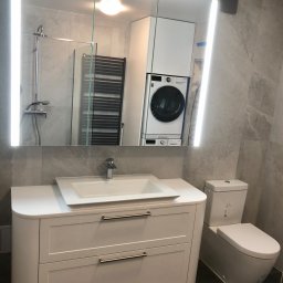 LAMAR meble - Nowoczesna łazienka z szafką pod umywalkę z szufladami, toaletą i lustrem z podświetleniem LED, w którym odbija się pralka i kabina prysznicowa.