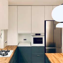 LAMAR meble - Nowoczesna kuchnia z białymi szafkami górnymi i szarymi dolnymi, drewniany blat, marmurowa podłoga. Widoczny piekarnik Bosch i lodówka side-by-side.