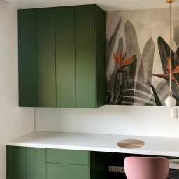 LAMAR meble - Zielone szafki kuchenne podwieszane i stojące z białym blatem, uzupełnione tapetą z motywem roślinnym i różowym krzesłem, tworzą nowoczesną przestrzeń do pracy.