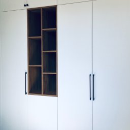 LAMAR meble - Biała szafa wnękowa z drewnianą, asymetryczną półką, czarne uchwyty, wzorzysta podłoga z płytek.