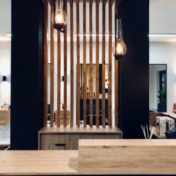 LAMAR meble - Nowoczesne wnętrze salonu fryzjerskiego z drewnianą recepcją, dekoracyjną ścianką z pionowych listew i wiszącymi lampami w stylu retro.