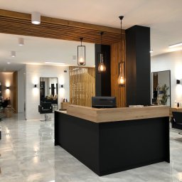 LAMAR meble - Nowoczesne wnętrze salonu fryzjerskiego z czarno-drewnianą recepcją, wiszącymi lampami w stylu loft, marmurową podłogą i drewnianymi panelami dekoracyjnymi.