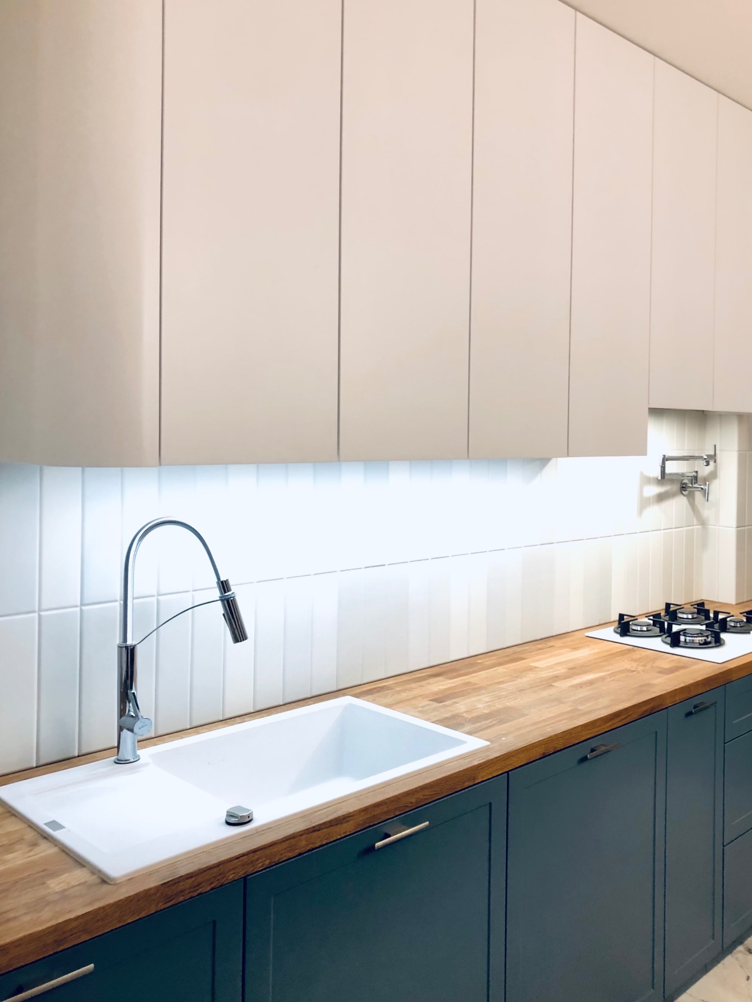 Nowoczesna kuchnia z drewnianym blatem, białym zlewem i ciemnymi szafkami. Uwagę przykuwa bateria z wyciąganą wylewką i minimalistyczny design.