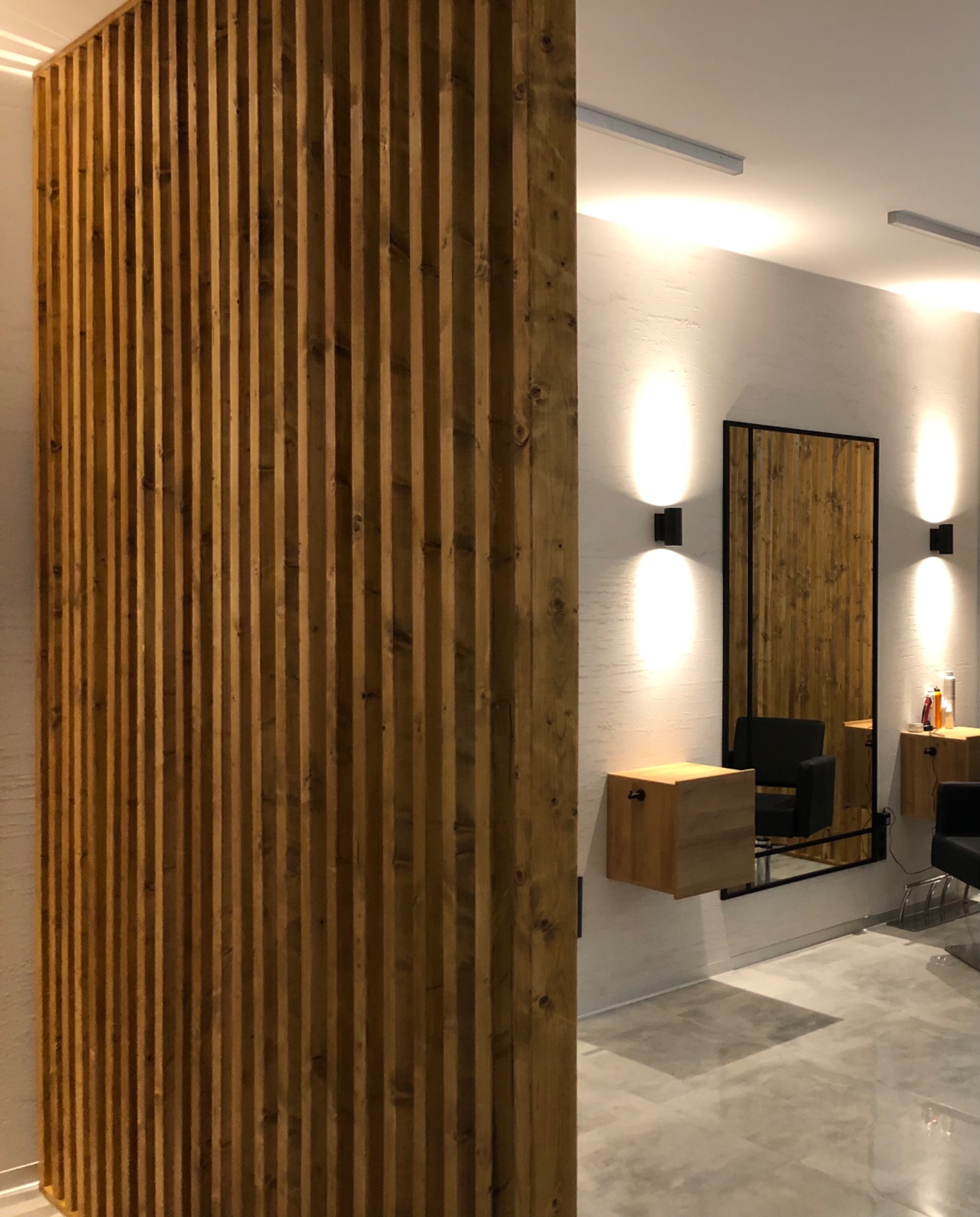 Drewniana ścianka działowa z pionowych listew w salonie fryzjerskim, widoczne lustra, oświetlenie punktowe i stanowiska pracy