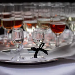 Uroczysty toast: Dwa kieliszki z kokardkami na srebrnej tacy, w tle rzędy wypełnionych kieliszków z różnymi napojami, tworzące elegancką kompozycję.