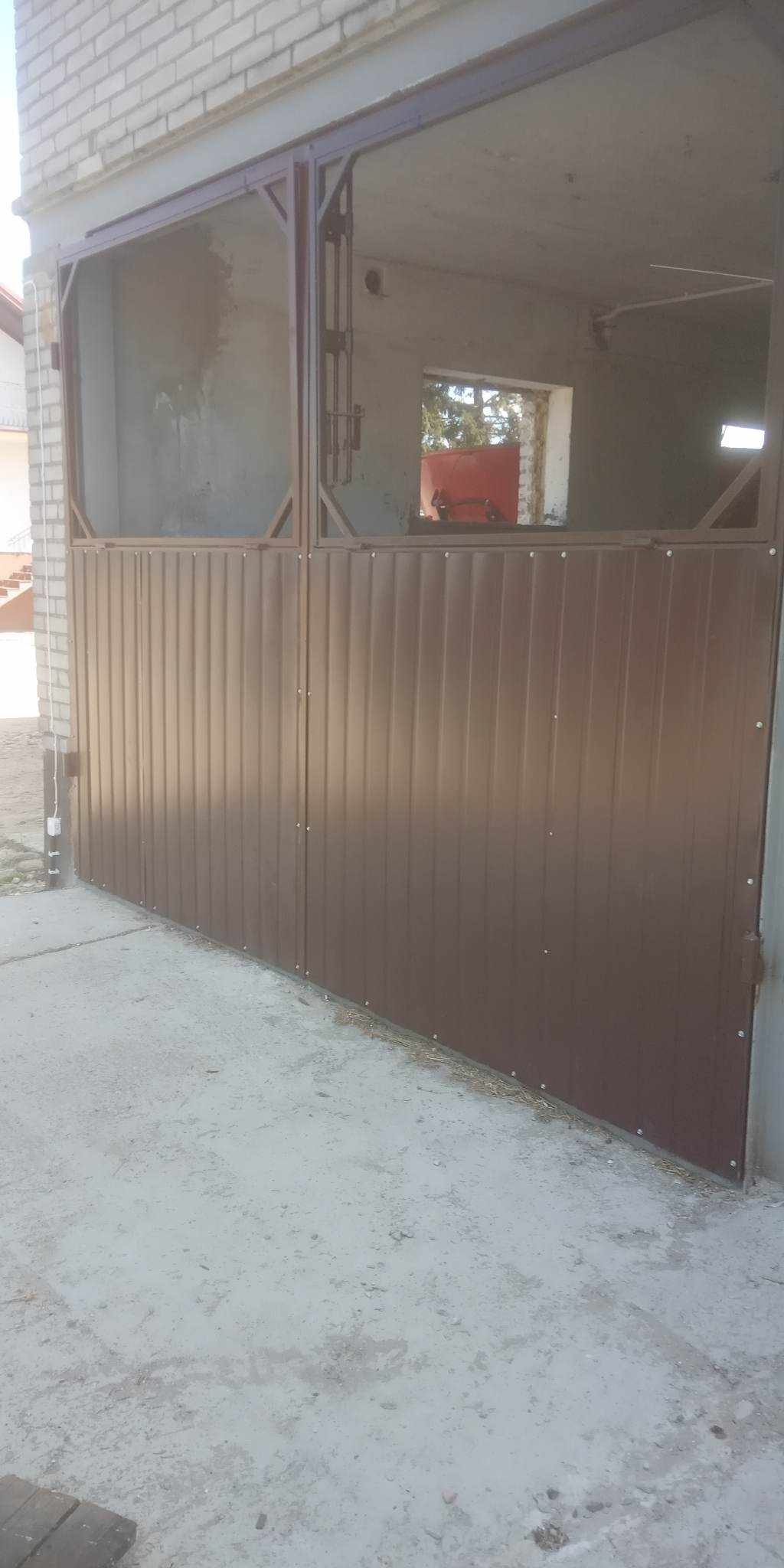 Brązowa brama wjazdowa z pionowymi panelami zamontowana w surowym otworze budynku z cegły i betonu, widoczne elementy konstrukcji metalowej.