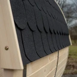 Fragment dachu sauny beczki pokrytego gontem bitumicznym w kolorze czarnym, widoczne jasne drewniane elementy konstrukcyjne i śruby mocujące.