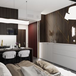 APART DESIGN - Nowoczesne studio z otwartą kuchnią, ciemnymi drewnianymi szafkami, białym marmurowym blatem, wyspą z szarymi krzesłami, oraz szafką RTV z dekoracyjną ścianą i poduszkami na pierwszym planie.