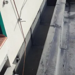 Szczegółowe ujęcie nowego, uszczelnionego dachu z blachy z widocznym systemem odprowadzania wody deszczowej przy ścianie budynku oraz przewodem odgromowym.