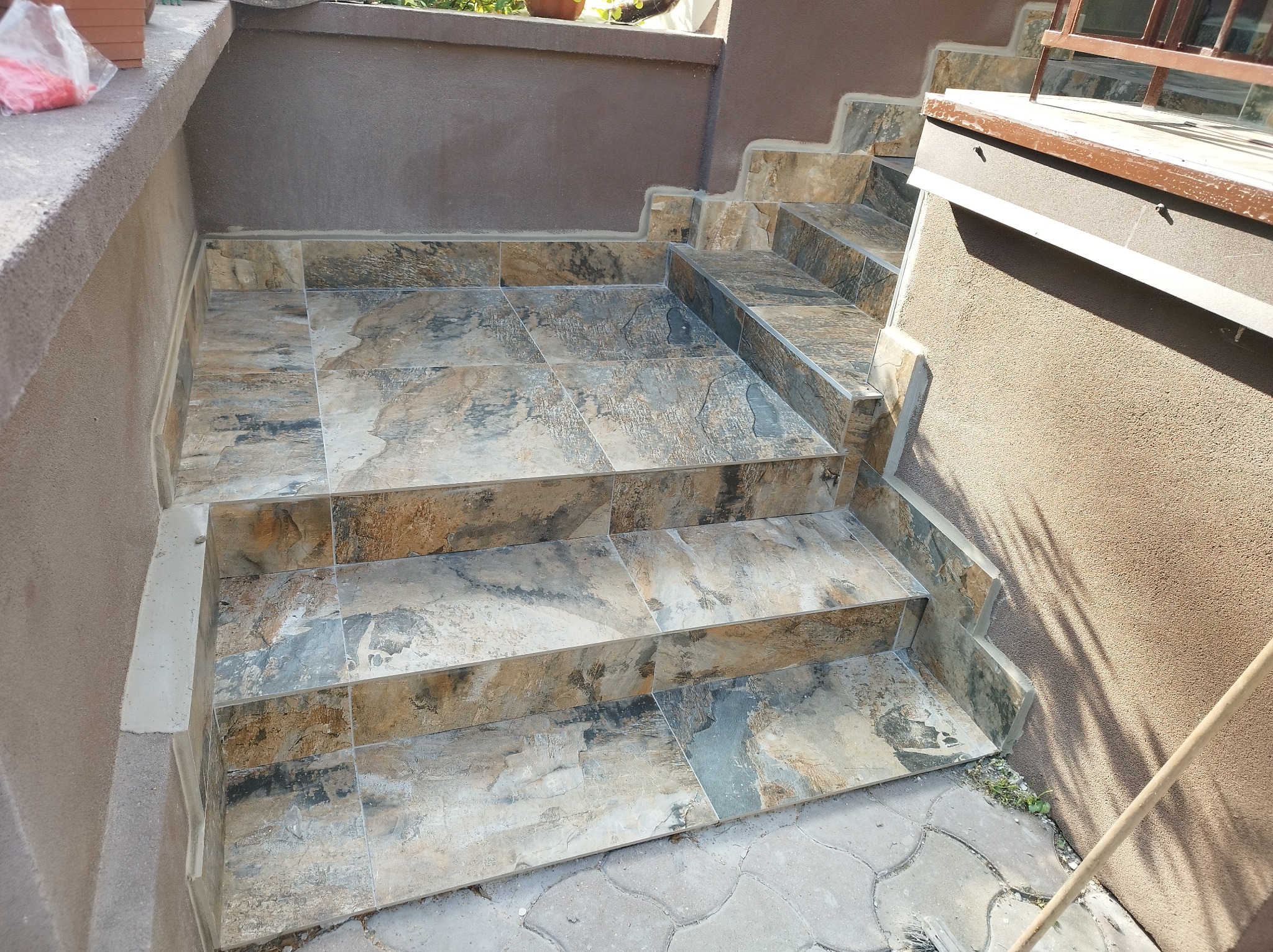 Wykończone schody zewnętrzne z płytek imitujących kamień, prowadzące do wejścia, z widocznymi detalami fug i faktury płytek.