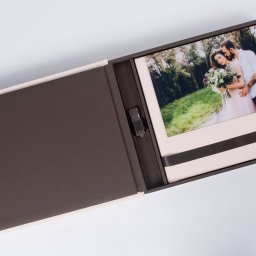 Marcin Konopnicki Portfolio - Otwarty, elegancki album fotograficzny z beżowo-brązowymi okładkami, zawierający zdjęcie pary młodej w plenerze oraz pendrive na czarnym pasku.