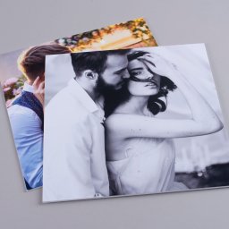 Marcin Konopnicki Portfolio - Dwa wydrukowane zdjęcia ślubne leżące na płaskiej powierzchni: jedno kolorowe z parą w ogrodzie, drugie czarno-białe z bliskim ujęciem pary.