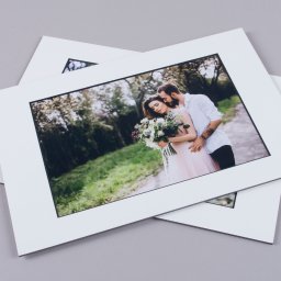 Marcin Konopnicki Portfolio - Dwa wydrukowane zdjęcia pary w objęciach, oprawione w białe ramki z czarną obwódką, leżące na szarym tle.