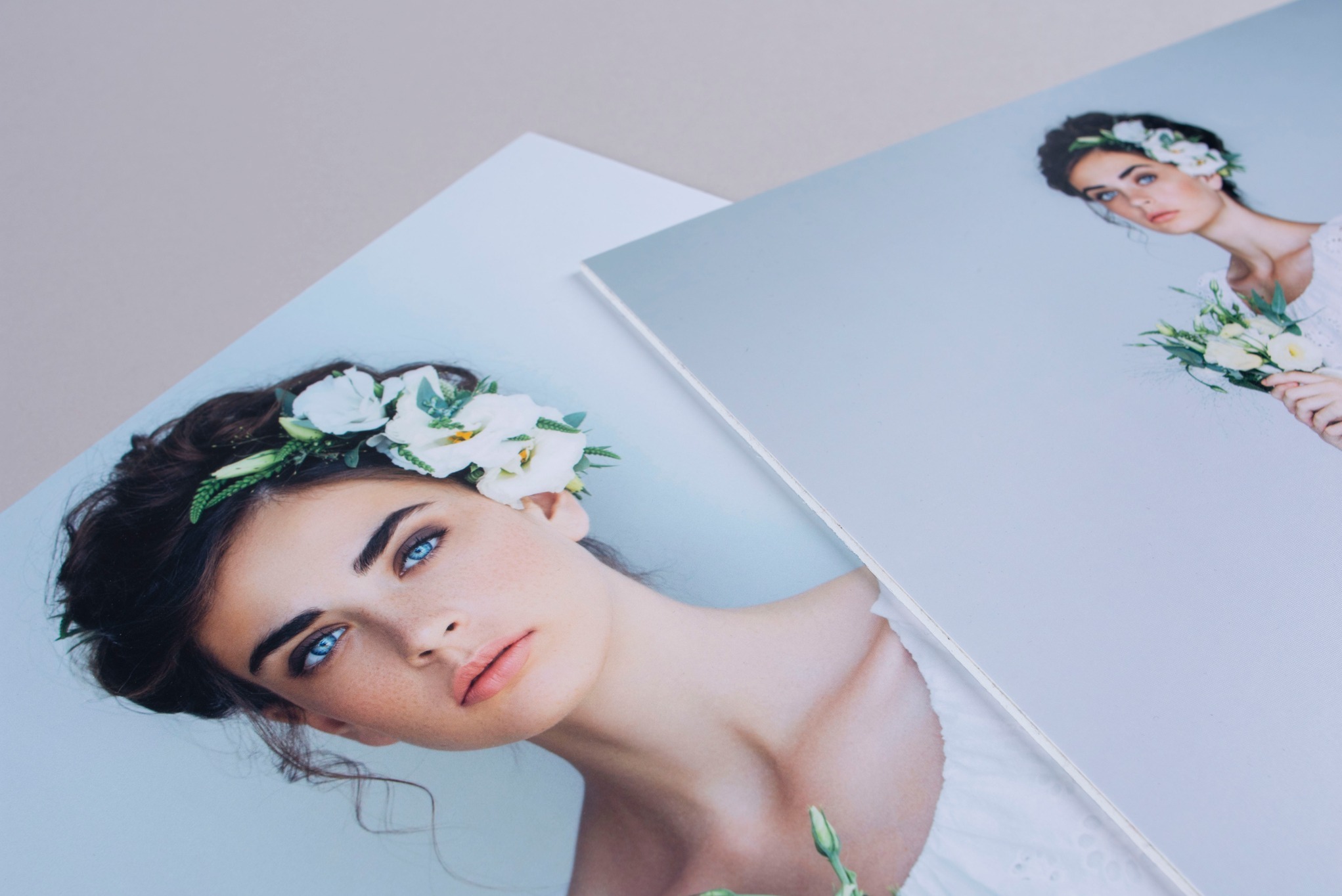 Dwa wydrukowane zdjęcia portretowe kobiety z kwiatami we włosach, ujęcie z bliska, widoczne detale makijażu i faktura papieru.