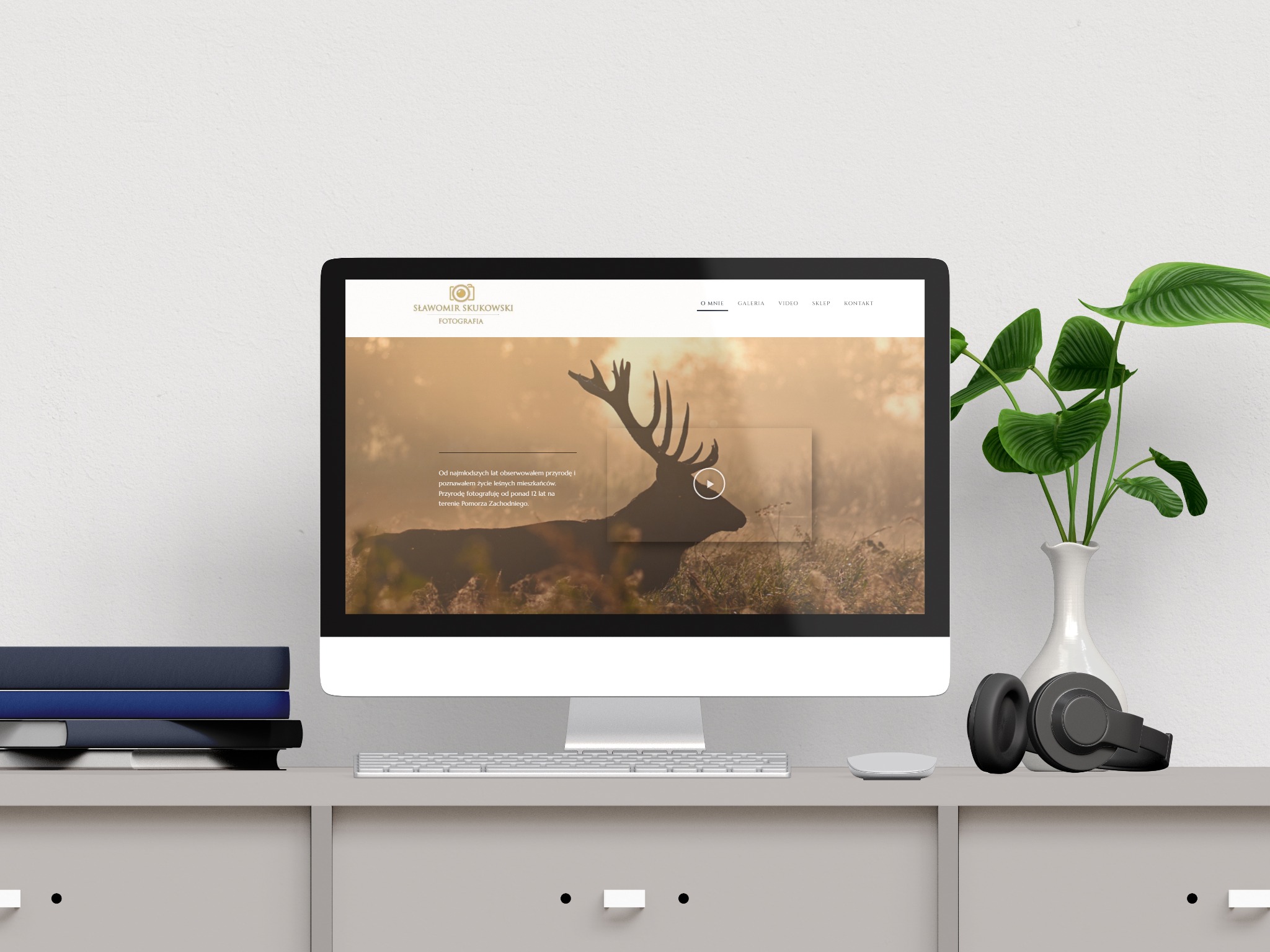 Monitor wyświetla stronę fotografa Sławomira Skukowskiego z motywem jelenia. Obok wazon z rośliną, słuchawki i myszka.