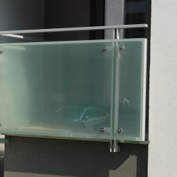 METAL-STYL Sp. z o.o. - Szklana balustrada balkonowa z widocznym samochodem za nią, mocowana na metalowych wspornikach do ściany budynku.