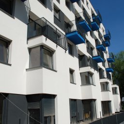 METAL-STYL Sp. z o.o. - Fasada budynku z balkonami z czarnymi balustradami i niebieskim spodem, widok z dołu na tle błękitnego nieba i drzew