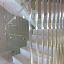 METAL-STYL Sp. z o.o. - Nowoczesne schody z kamiennymi stopniami, zabezpieczone szklaną balustradą z drewnianą poręczą i pionowymi, metalowymi prętami.