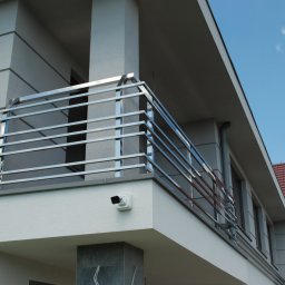 METAL-STYL Sp. z o.o. - Nowoczesna balustrada balkonowa ze stali nierdzewnej z poziomymi prętami, zamontowana na jasnym budynku z widoczną kamerą monitoringu.