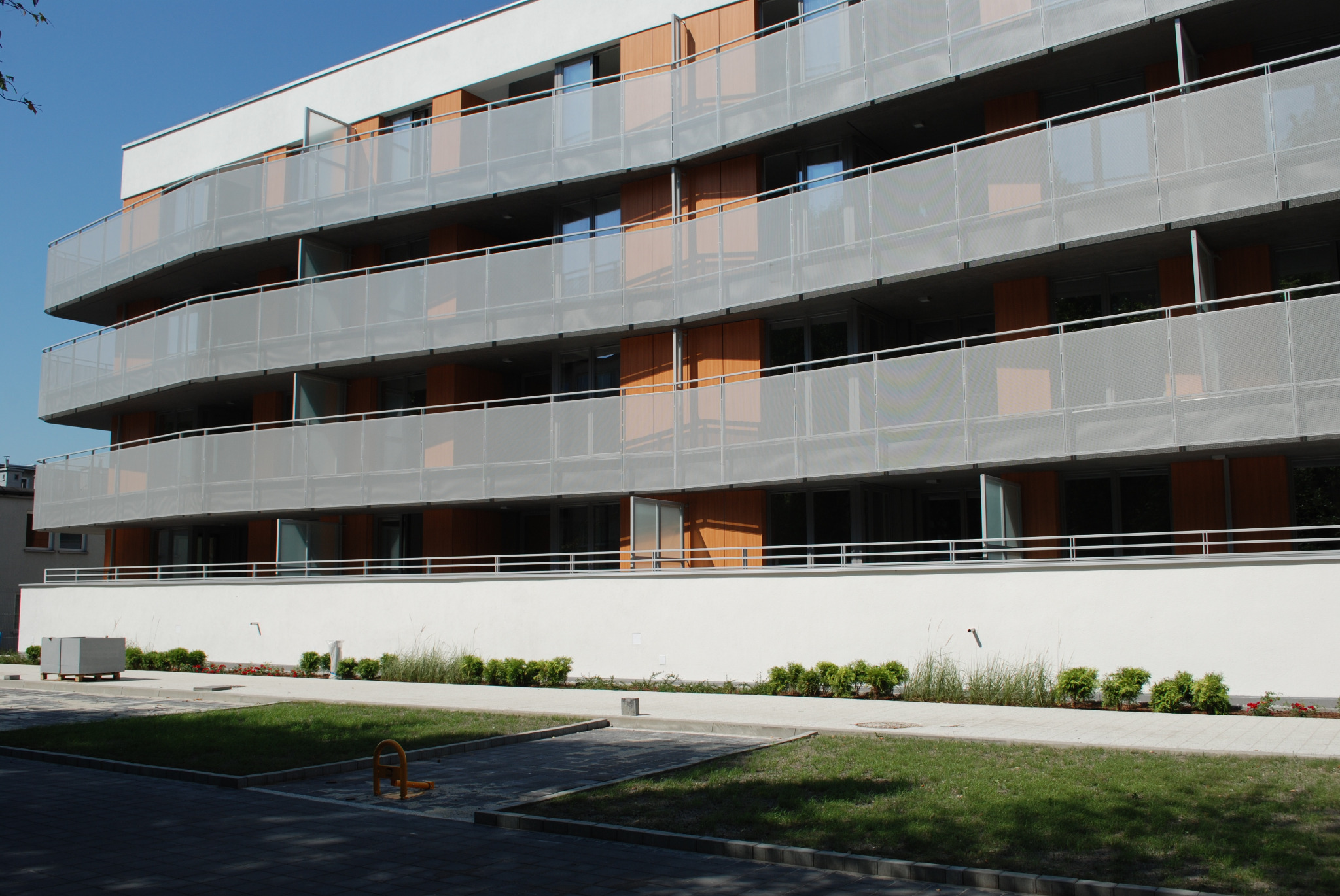 Nowoczesny budynek apartamentowy z balkonami zabezpieczonymi ażurowymi, metalowymi barierkami, widok z poziomu chodnika.