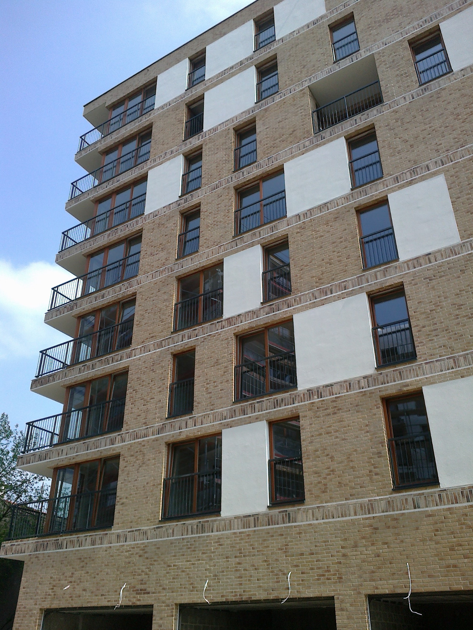 Wielopiętrowy budynek z cegły z balkonami z czarnymi, metalowymi balustradami, widziany z dołu pod kątem.