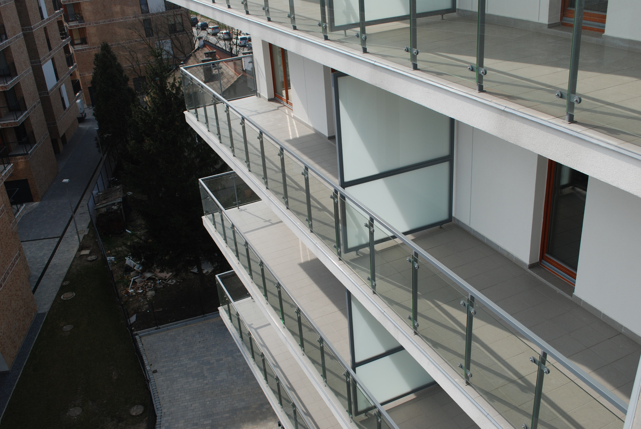 Wielopiętrowy budynek z balkonami zabezpieczonymi szklanymi balustradami z nierdzewnymi elementami mocującymi, widok z góry.