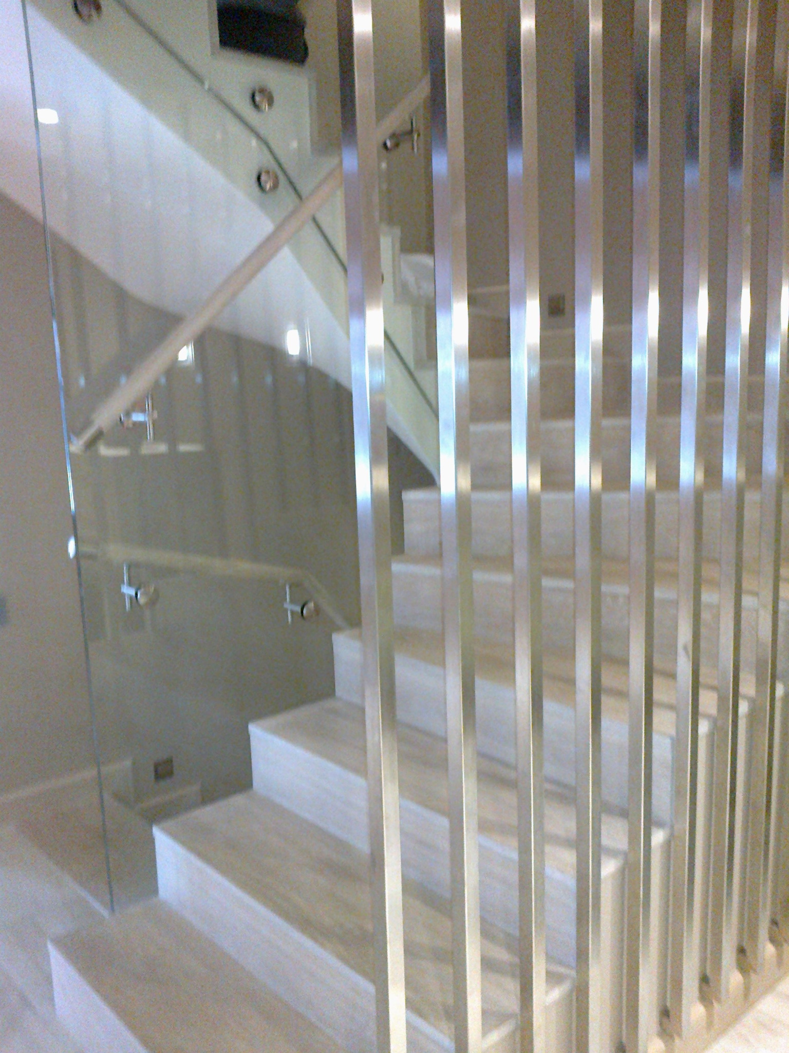 Nowoczesne schody z kamiennymi stopniami, zabezpieczone szklaną balustradą z drewnianą poręczą i pionowymi, metalowymi prętami.