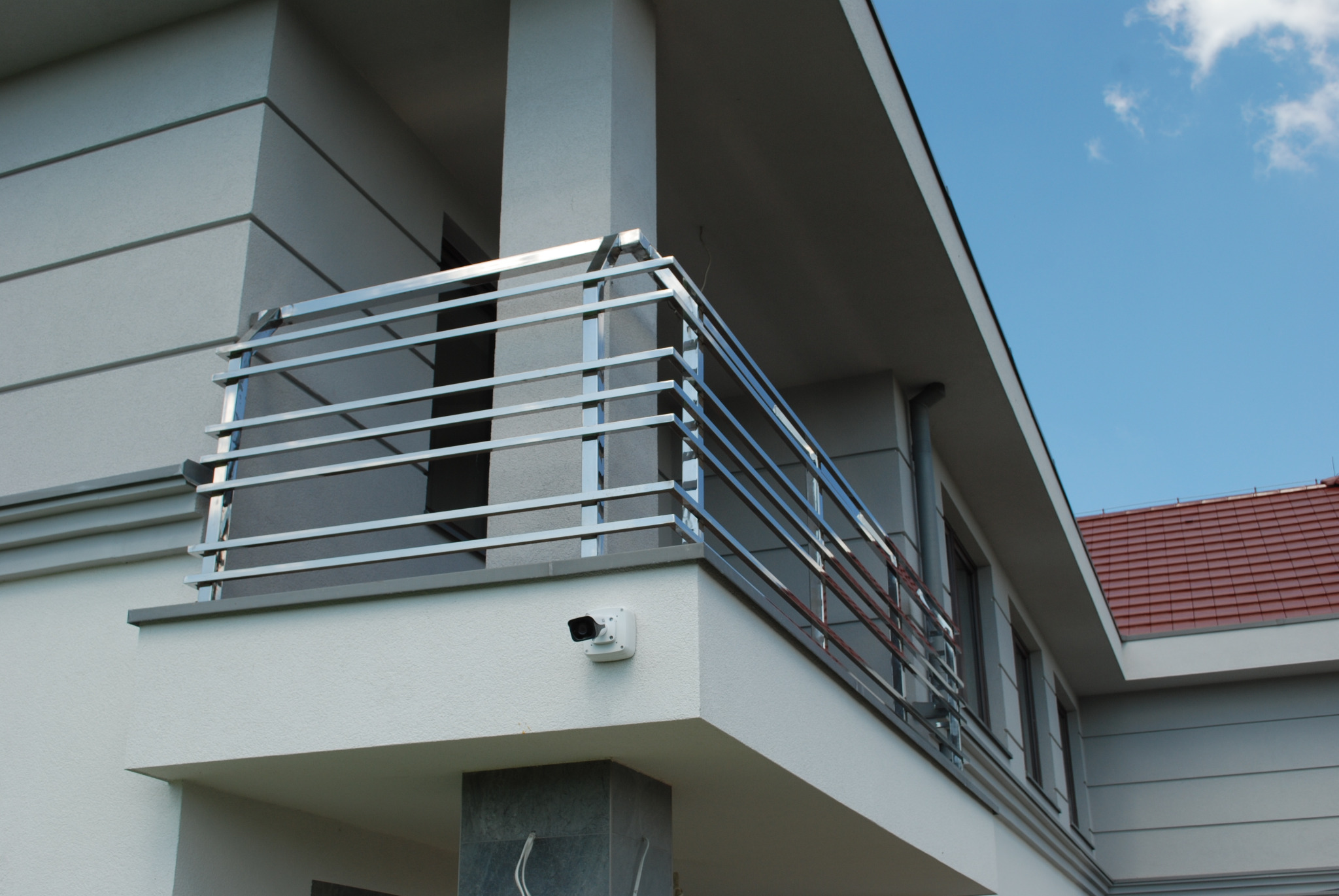 Nowoczesna balustrada balkonowa ze stali nierdzewnej z poziomymi prętami, zamontowana na jasnym budynku z widoczną kamerą monitoringu.
