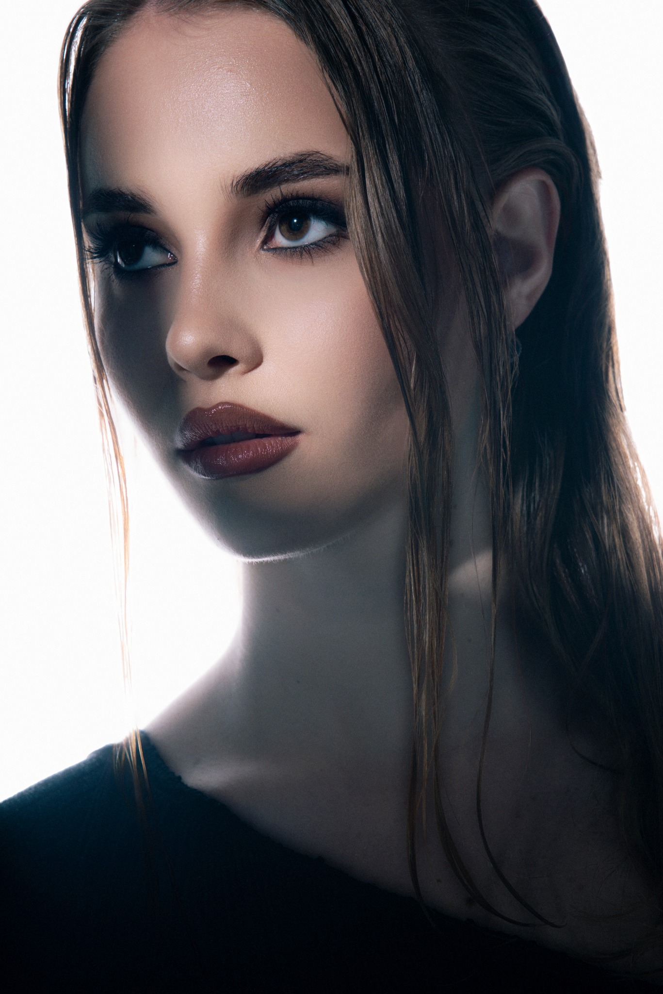 Portret kobiety z mokrymi włosami, z profilu, z mocnym makijażem oczu i ust, oświetlona od tyłu, z widocznym delikatnym meszkiem na policzku.