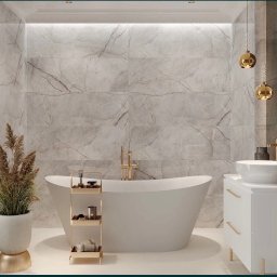 Kompleksowy Remont - Elegancka łazienka z marmurowymi płytkami ściennymi, wolnostojącą białą wanną, złotą armaturą i dekoracyjnymi lampami wiszącymi, uzupełniona o białą szafkę umywalkową i roślinę w doniczce na złotym...