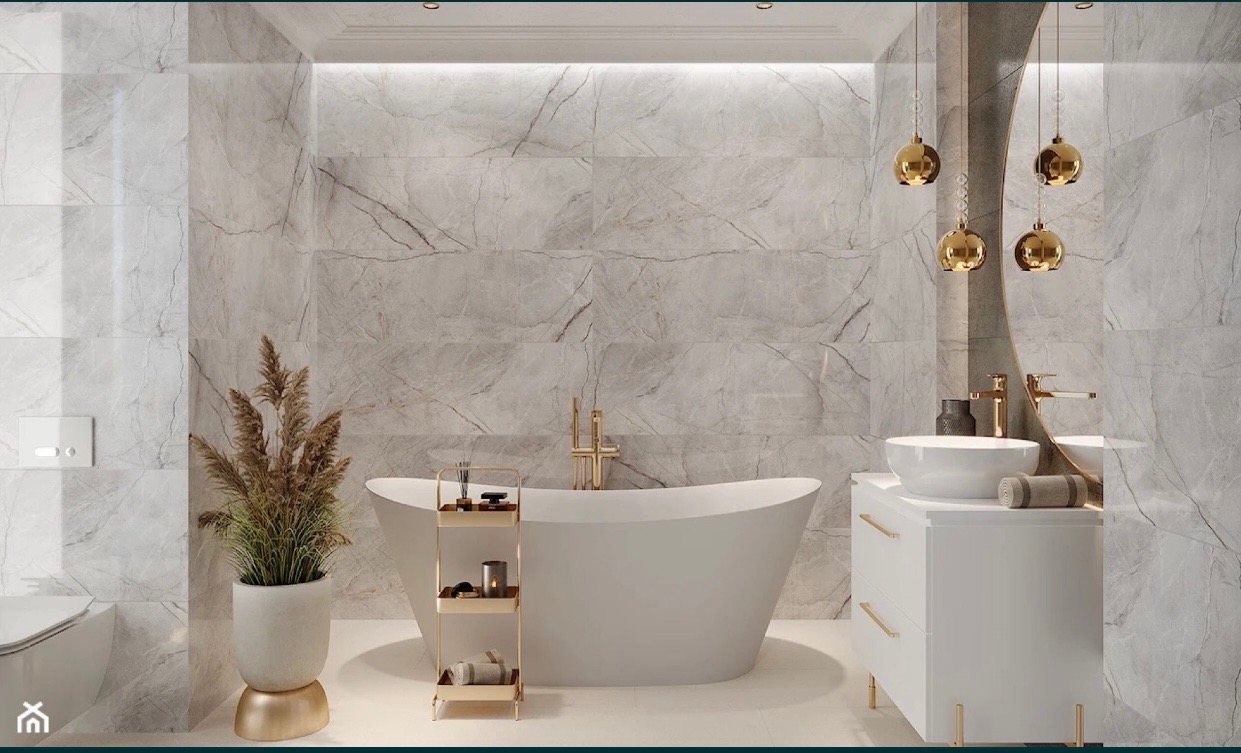 Elegancka łazienka z marmurowymi płytkami ściennymi, wolnostojącą białą wanną, złotą armaturą i dekoracyjnymi lampami wiszącymi, uzupełniona o białą szafkę umywalkową i roślinę w doniczce na złotym...