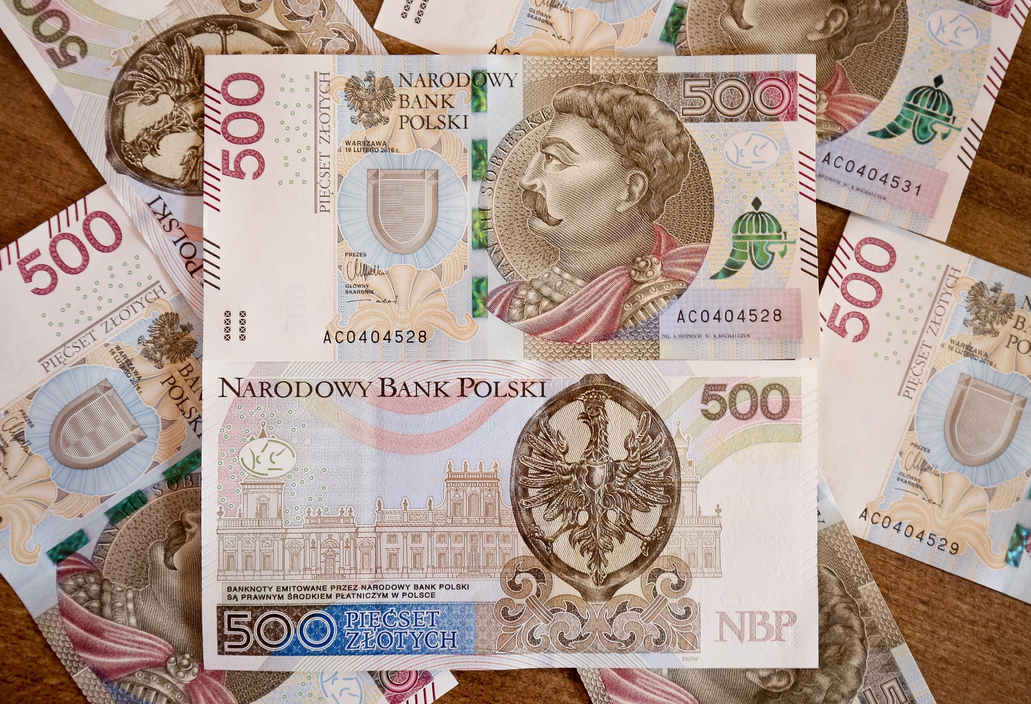 Stos banknotów 500 zł z wizerunkiem Jana III Sobieskiego i orła w koronie, ułożonych na drewnianej powierzchni.