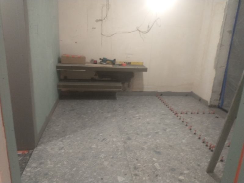 Łazienka w trakcie remontu: ułożona szara terakota podłogowa z krzyżykami dystansowymi, widoczne narzędzia na półce, ściany przygotowane do malowania.