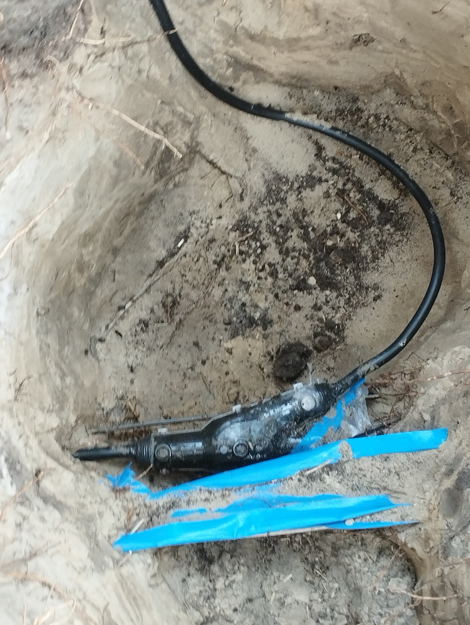 Podziemne przyłącze elektryczne w wykopie, z widocznym kablem i niebieską folią ochronną.