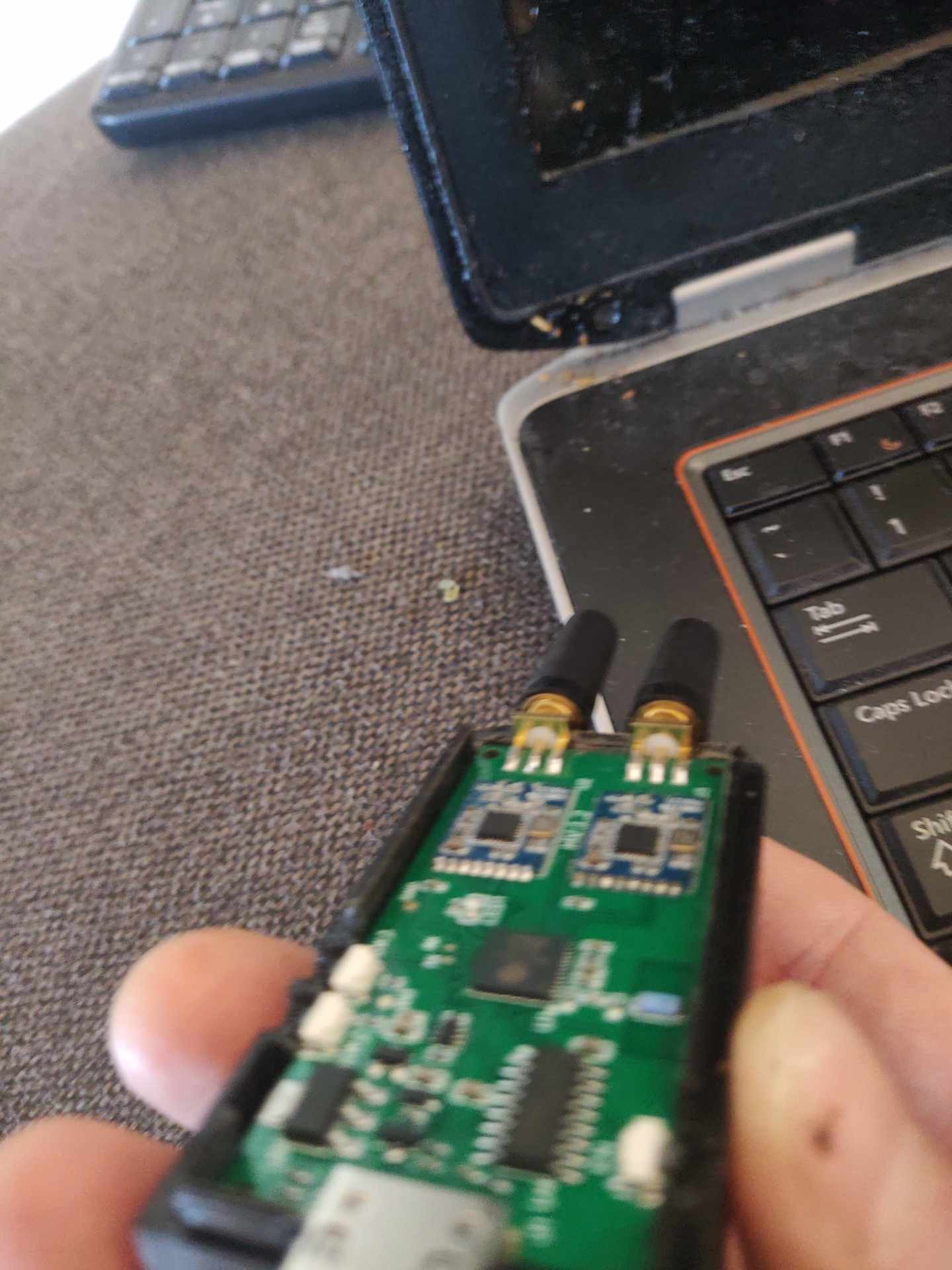 Otwarta obudowa krótkofalówki z widoczną płytką drukowaną, leżąca na brudnym laptopie i szarej kanapie.