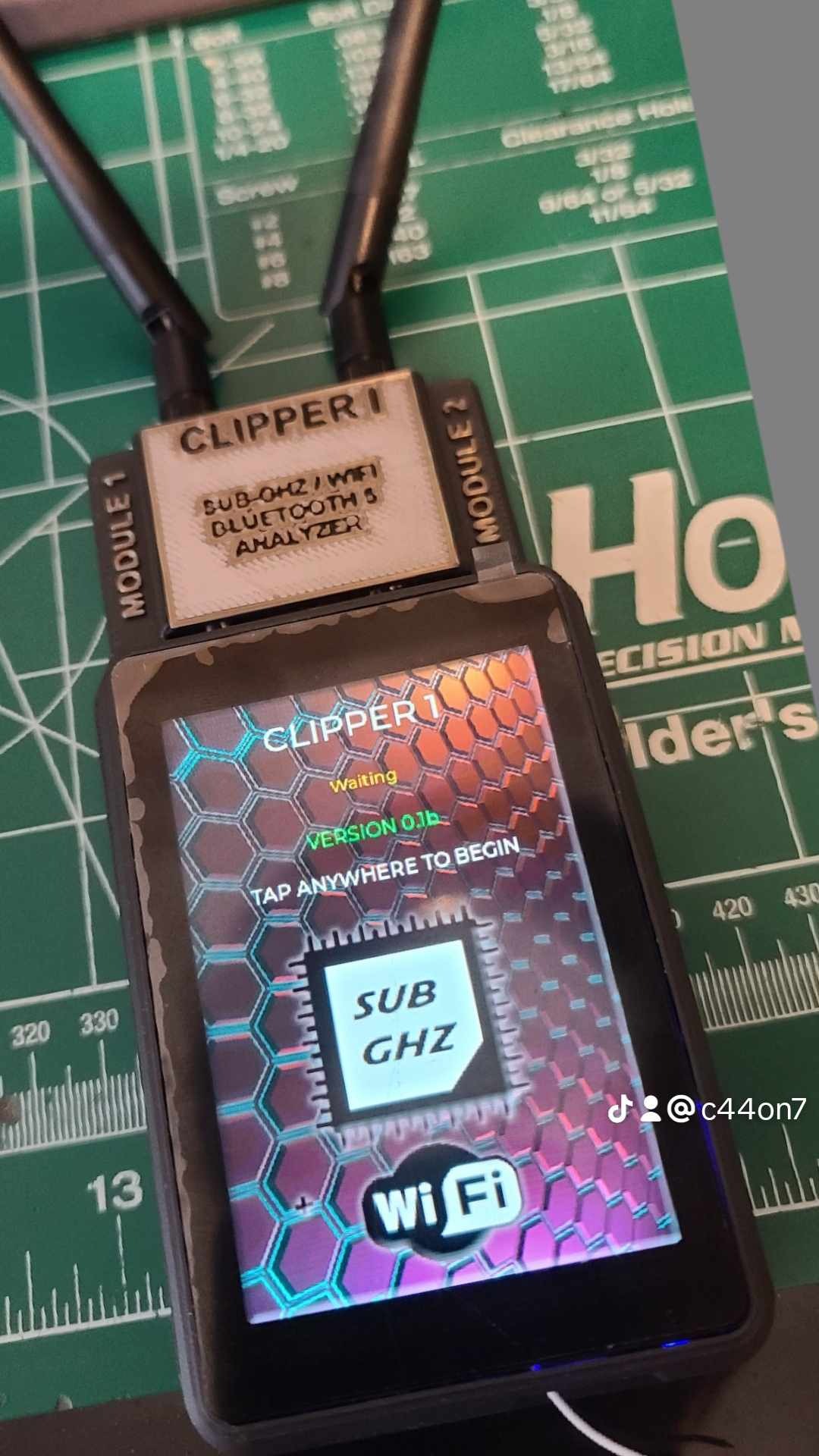 Urządzenie Clipper 1 z dwoma antenami, analizujące Sub-GHz, WiFi i Bluetooth 5, wyświetlające komunikat 'Waiting' na ekranie, umieszczone na macie pomiarowej.