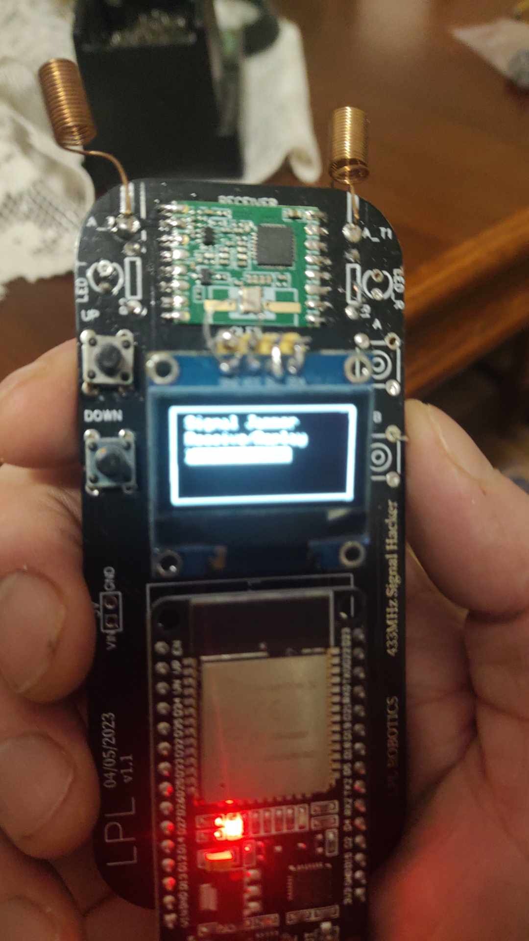 Prototyp urządzenia do analizy sygnałów 433MHz z wyświetlaczem pokazującym 'Signal Jammer Detection Display', widoczne elementy elektroniczne, anteny spiralne, przyciski oraz dioda LED