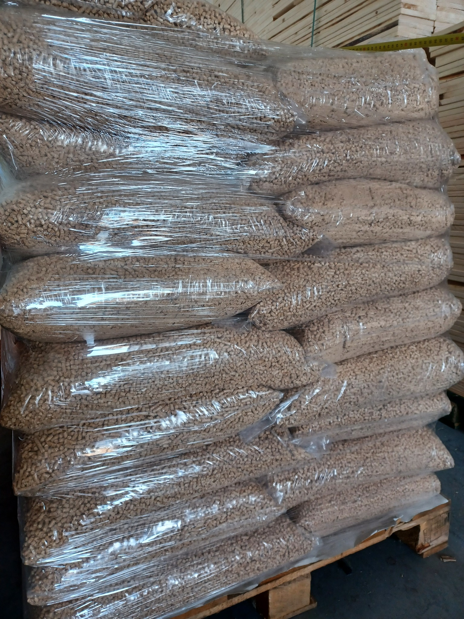 Paleta z workami pelletu drzewnego, owinięta folią stretch, ułożona w stos, widoczne deski w tle.