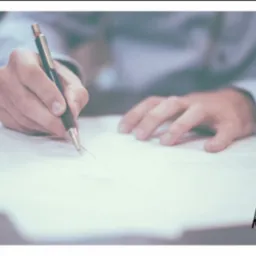 Osoba w jasnej koszuli podpisuje dokument czarnym piórem na stole, w prawym dolnym rogu widoczne logo firmy.