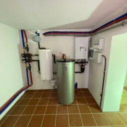 Zainstalowana instalacja grzewcza z dwoma zbiornikami: biały i srebrny Puretherm, liczne rury w kolorach niebieskim i czerwonym, oraz biała skrzynka sterownicza na ścianie w pomieszczeniu z brązową...