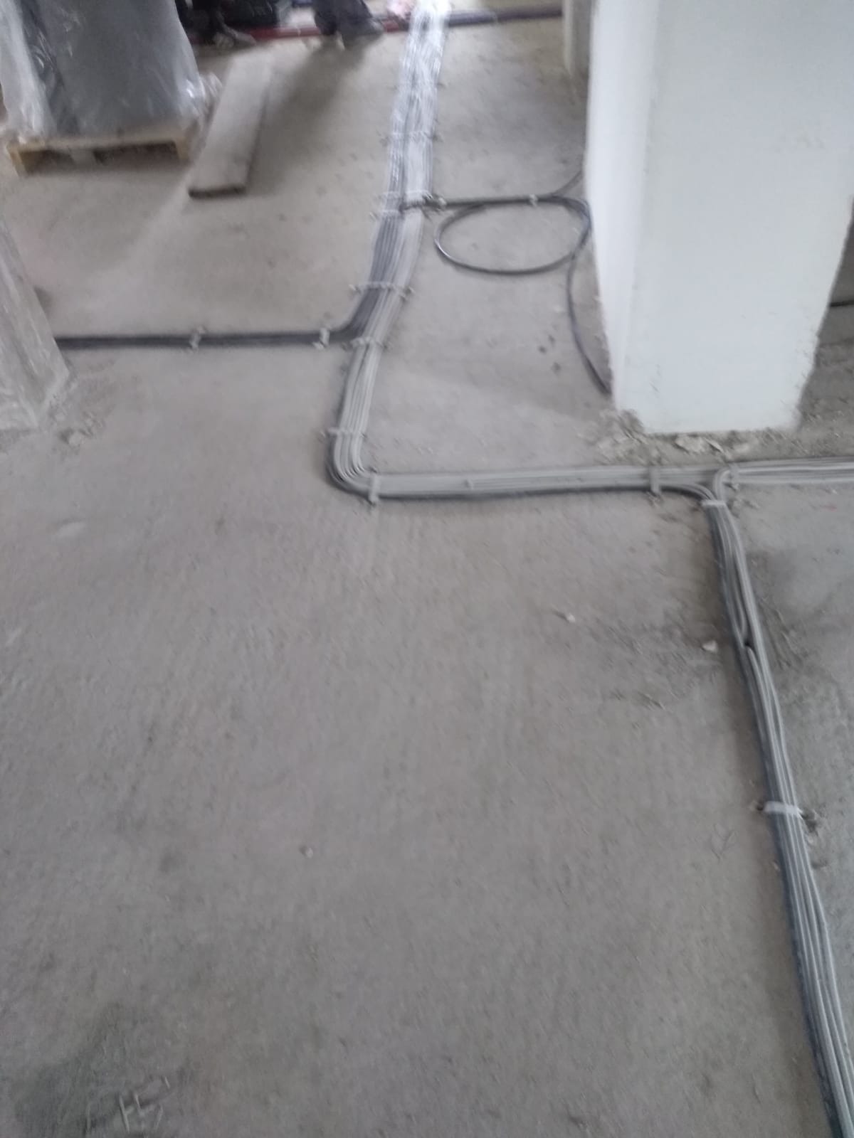 Szare kable elektryczne ułożone na surowym betonowym podłożu w trakcie instalacji, widoczne uchwyty mocujące kable do podłoża.