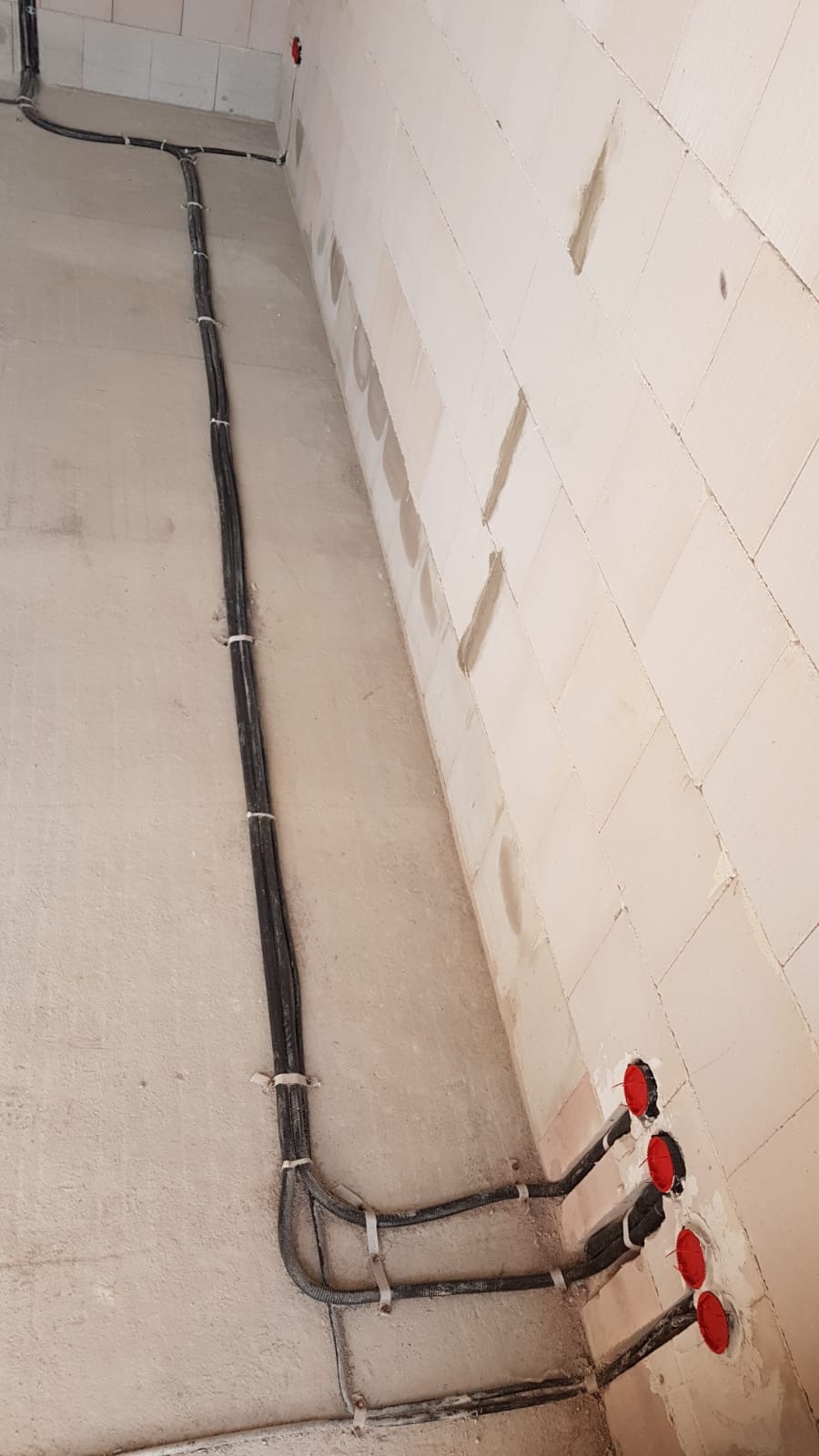 Ściana z betonu komórkowego z poprowadzonymi przewodami elektrycznymi w peszlach, zamocowanymi uchwytami, widoczne puszki instalacyjne z czerwonymi zaślepkami.
