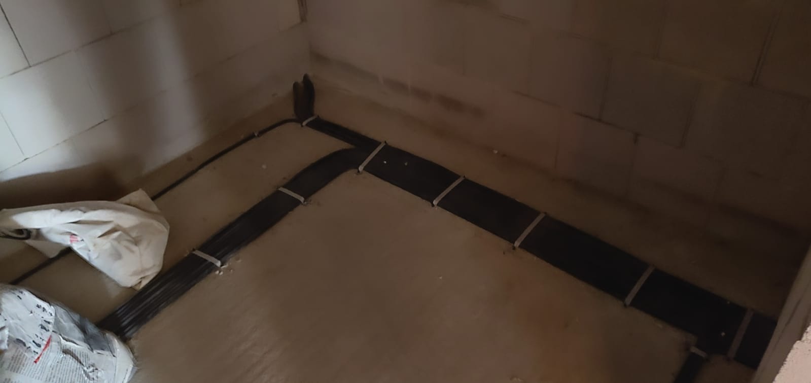 Kable elektryczne ułożone wzdłuż ściany w surowym stanie, zabezpieczone paskami mocującymi, widoczne ślady montażu i pozostałości materiałów budowlanych.