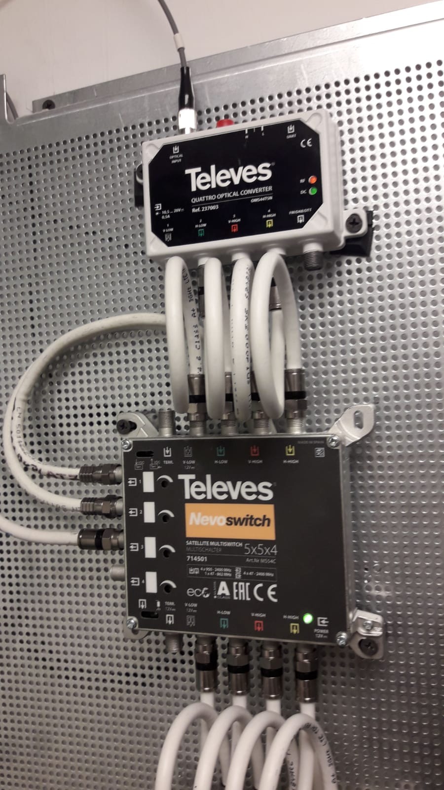 Konwerter optyczny i multiswitch satelitarny Televes zamontowane na perforowanej płycie, z podłączonymi kablami koncentrycznymi.