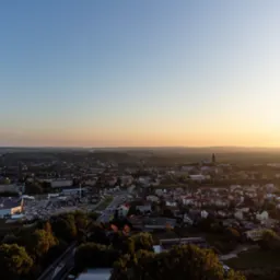 Panorama miasta z lotu ptaka o wschodzie słońca, widoczne budynki mieszkalne, sklepy i kościół w oddali.