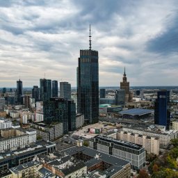 KrzysiekAirborne - Panorama Warszawy z lotu ptaka, widok na drapacze chmur w pochmurny dzień, w tle Pałac Kultury i Nauki.